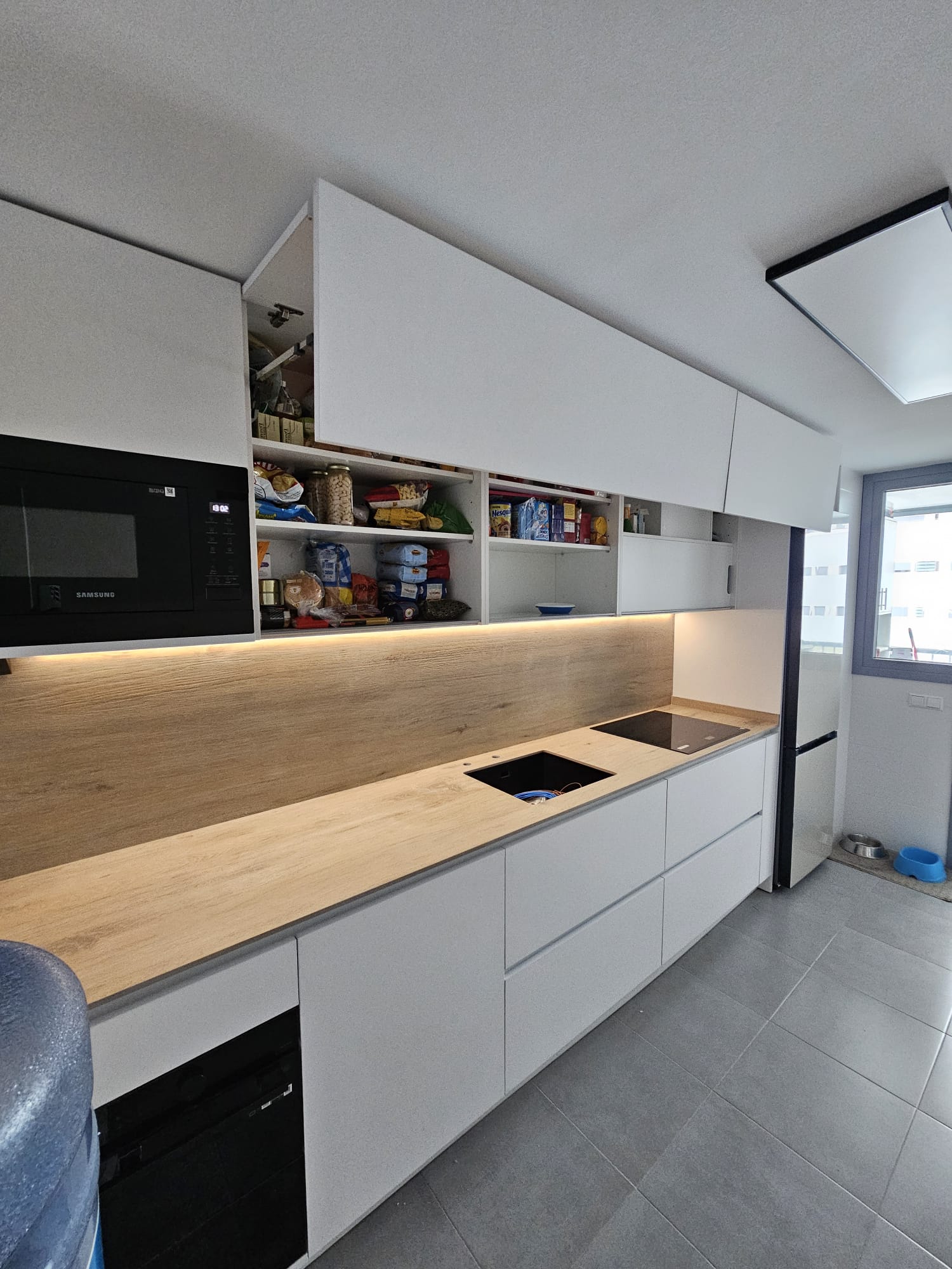Cocina blanca con encimera y frente de roble e iluminación bajo muebles