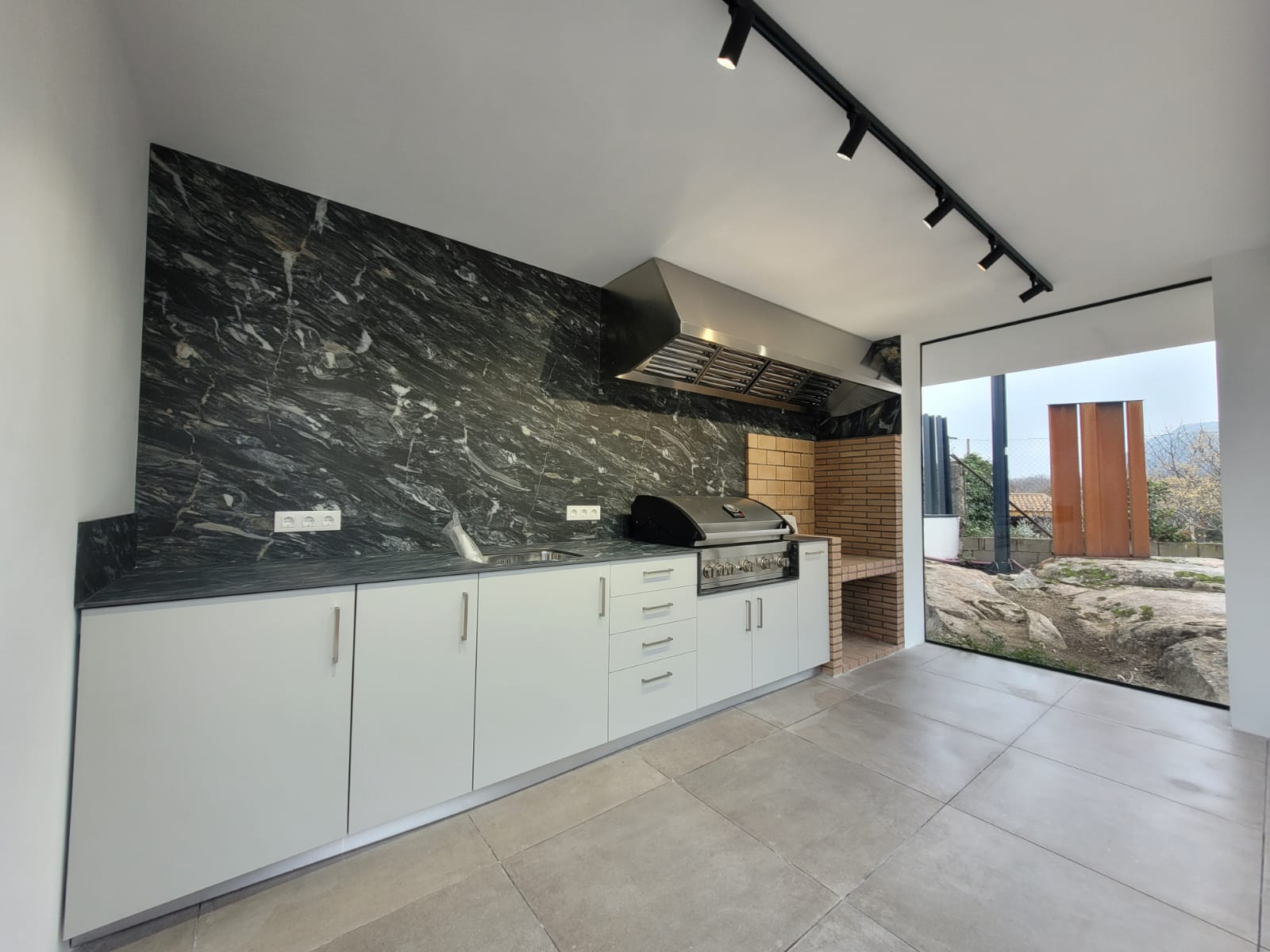 Cocina de exterior con frente de piedra oscura y barbacoa